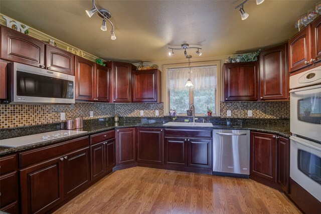 kitchen with dark stone countertops, light hardwood / wood-style flooring, decorative light fixtures, appliances with stainless steel finishes, and sink