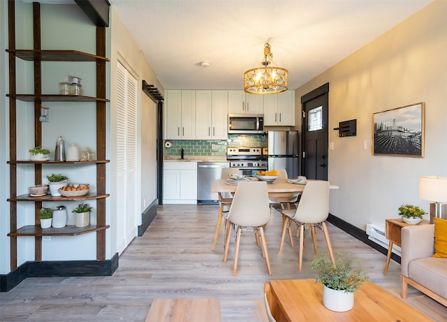 kitchen with appliances with stainless steel finishes, light hardwood / wood-style flooring, decorative light fixtures, white cabinetry, and backsplash