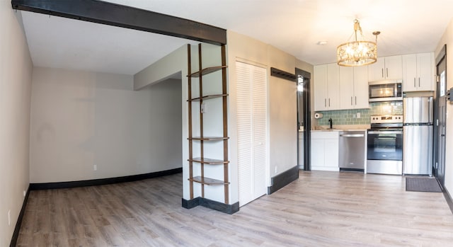 kitchen featuring white cabinets, light wood-type flooring, decorative backsplash, and stainless steel appliances