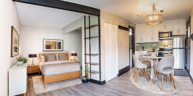 bedroom featuring stainless steel fridge, a closet, an inviting chandelier, and light wood-type flooring