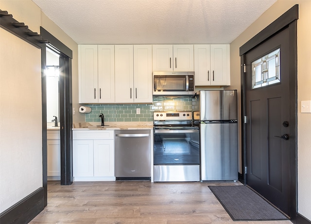 kitchen with stainless steel appliances, tasteful backsplash, sink, light wood-type flooring, and white cabinets