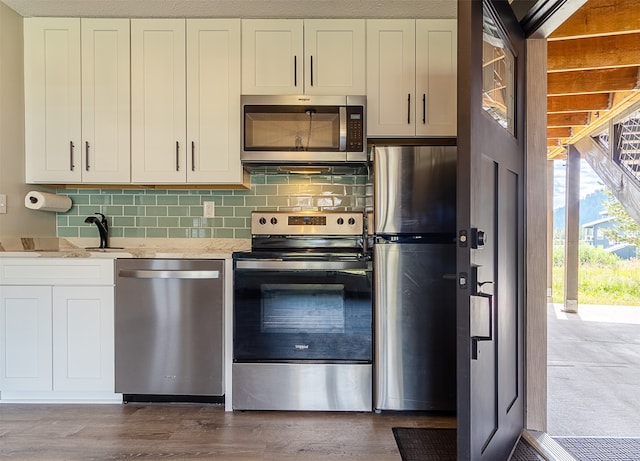 kitchen featuring wood-type flooring, light stone counters, decorative backsplash, and stainless steel appliances