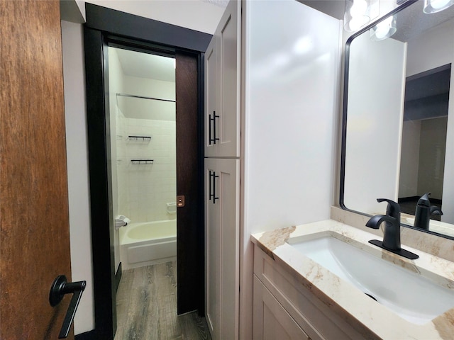 bathroom with hardwood / wood-style floors, tiled shower / bath combo, and vanity