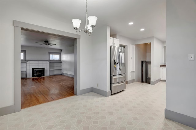 kitchen with stainless steel fridge, ceiling fan with notable chandelier, a fireplace, white cabinets, and decorative light fixtures