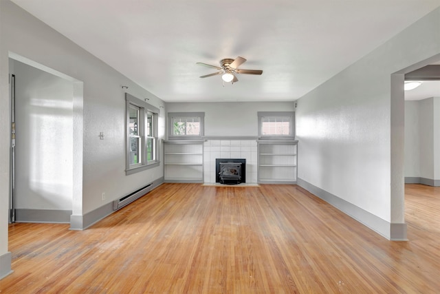 unfurnished living room featuring baseboard heating, ceiling fan, light hardwood / wood-style flooring, and a wood stove