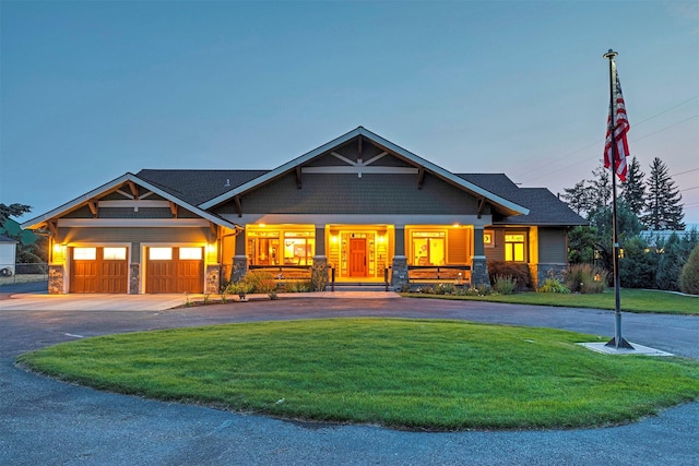 craftsman inspired home featuring covered porch, a garage, stone siding, driveway, and a front lawn