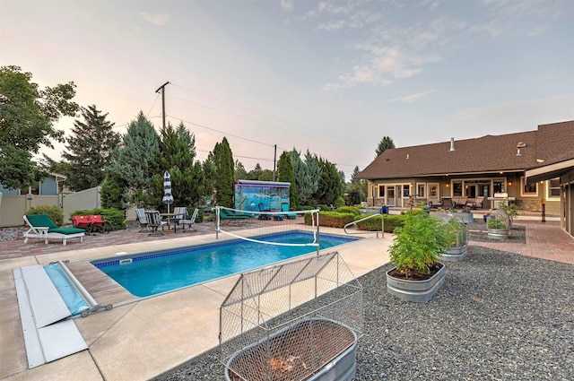 pool at dusk featuring an outdoor pool, a patio, and fence