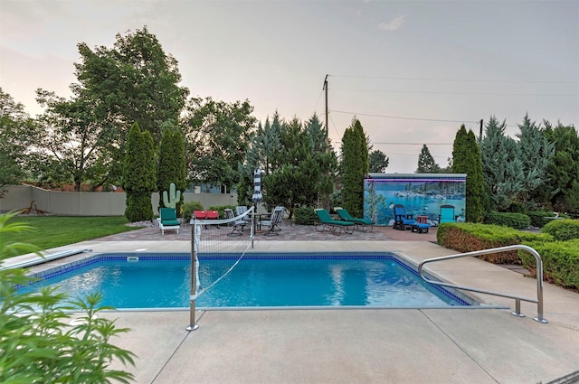 pool at dusk with a patio area, fence, and an outdoor pool