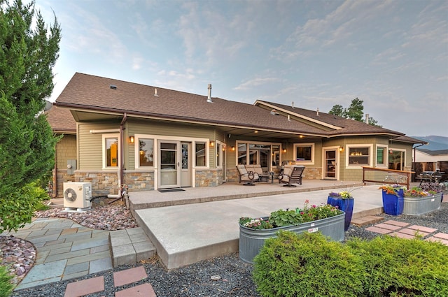 back of house with ac unit, roof with shingles, a patio, stone siding, and an outdoor living space