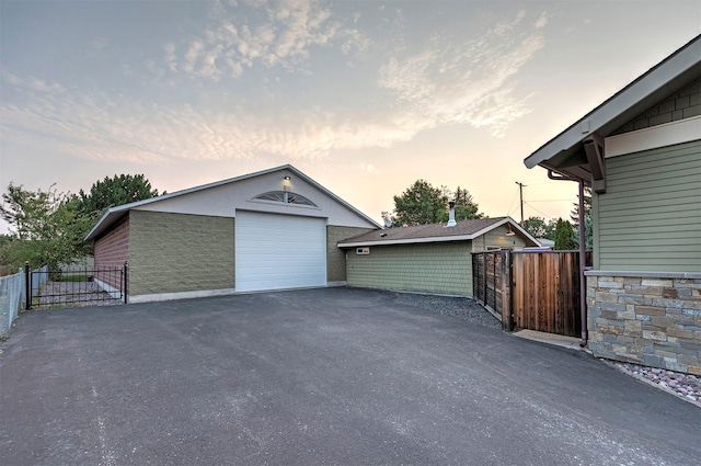 garage at dusk with a garage, aphalt driveway, fence, and a gate