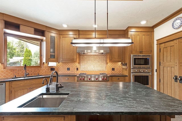 kitchen with appliances with stainless steel finishes, brown cabinetry, a sink, and an island with sink