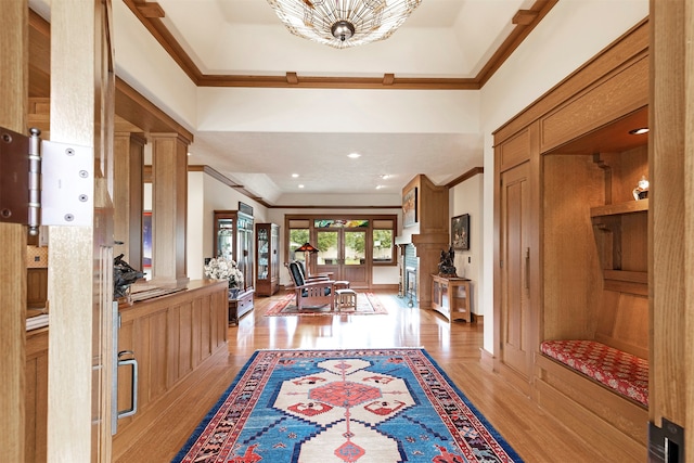 foyer entrance featuring ornate columns, a raised ceiling, crown molding, and light hardwood / wood-style flooring