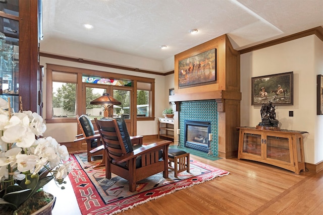 living area featuring a textured ceiling, a fireplace, wood finished floors, and crown molding