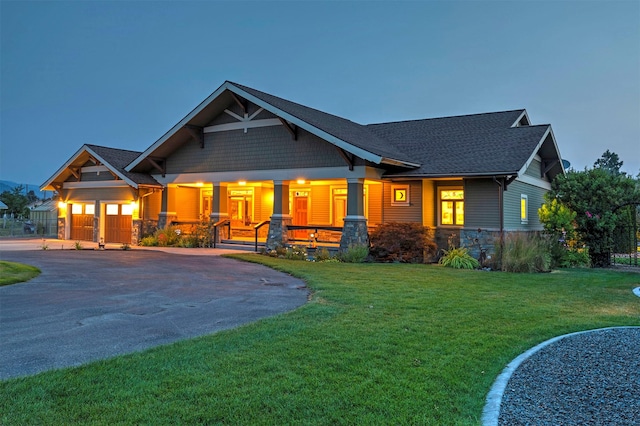 view of front of house with a porch, an attached garage, stone siding, driveway, and a front lawn