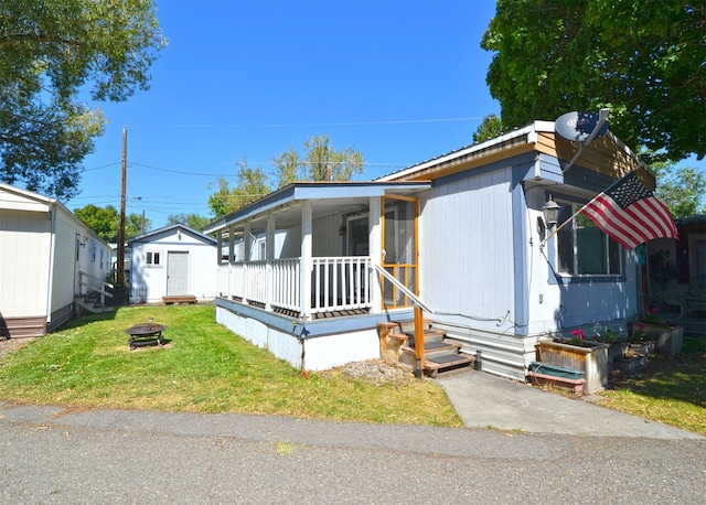 view of front facade with a shed, a porch, a fire pit, and a front yard