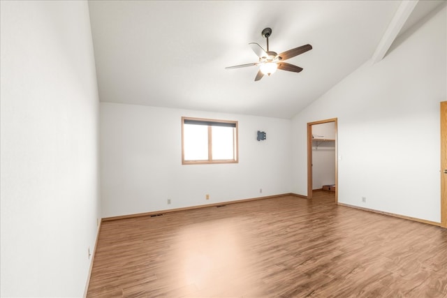 empty room featuring visible vents, a ceiling fan, vaulted ceiling, wood finished floors, and baseboards