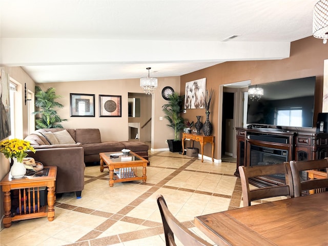 living area with visible vents, a notable chandelier, a glass covered fireplace, baseboards, and vaulted ceiling