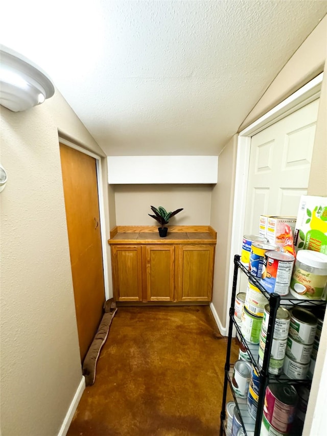 hallway featuring a textured ceiling, baseboards, and vaulted ceiling