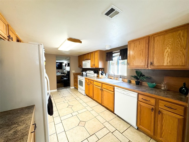 kitchen featuring white appliances, light tile patterned floors, visible vents, a sink, and dark countertops