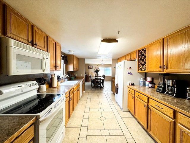 kitchen featuring a sink, white appliances, an inviting chandelier, light tile patterned flooring, and brown cabinetry