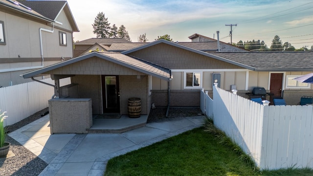 rear view of property featuring a patio, fence private yard, and roof with shingles