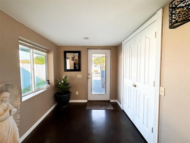 doorway with a healthy amount of sunlight, concrete flooring, and baseboards