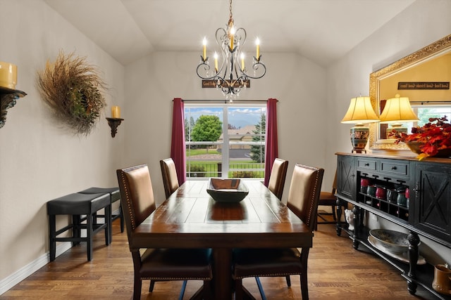 dining space featuring hardwood / wood-style floors, vaulted ceiling, and an inviting chandelier