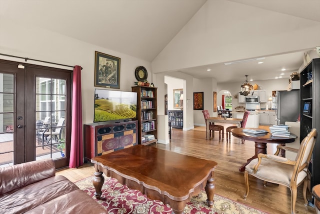 living room featuring high vaulted ceiling, plenty of natural light, light hardwood / wood-style flooring, and french doors