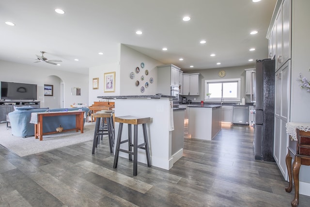 kitchen with dark hardwood / wood-style floors, a breakfast bar area, ceiling fan, a kitchen island, and stainless steel dishwasher