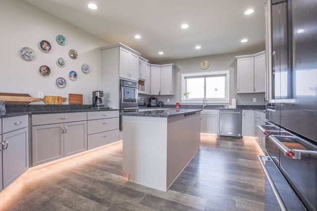 kitchen featuring dark hardwood / wood-style flooring, appliances with stainless steel finishes, a center island, dark stone countertops, and white cabinets