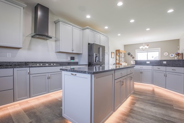 kitchen featuring an inviting chandelier, light wood-type flooring, appliances with stainless steel finishes, wall chimney range hood, and dark stone counters