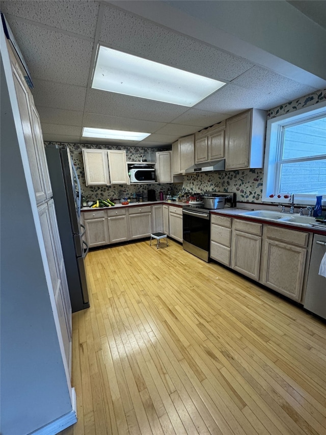 kitchen featuring stainless steel appliances, decorative backsplash, light wood-style floors, a sink, and under cabinet range hood