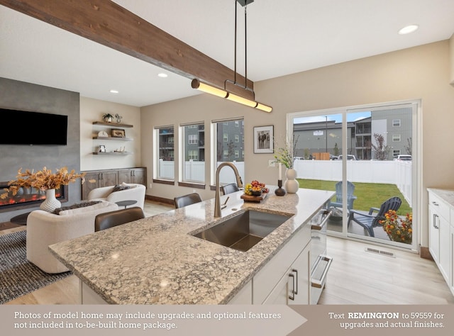 kitchen featuring light stone counters, sink, a center island with sink, white cabinets, and hanging light fixtures