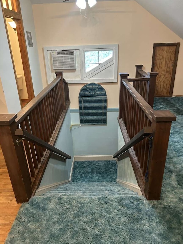 stairway with a wall mounted AC, ceiling fan, hardwood / wood-style floors, and vaulted ceiling