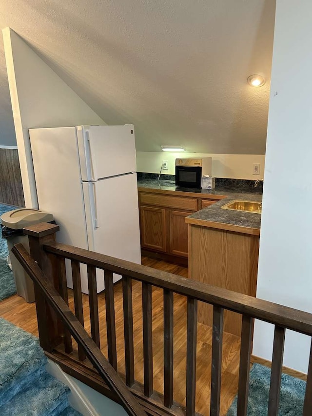 kitchen with white refrigerator, a textured ceiling, wood-type flooring, and vaulted ceiling