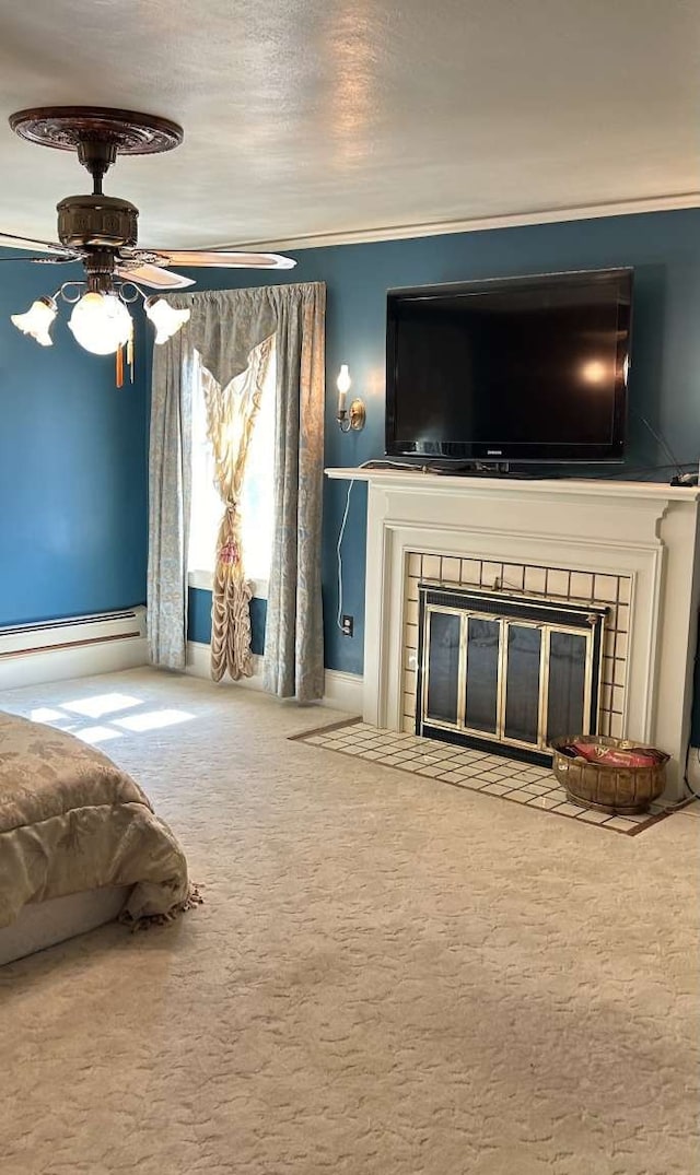 unfurnished bedroom featuring a tiled fireplace, crown molding, ceiling fan, carpet, and a baseboard heating unit