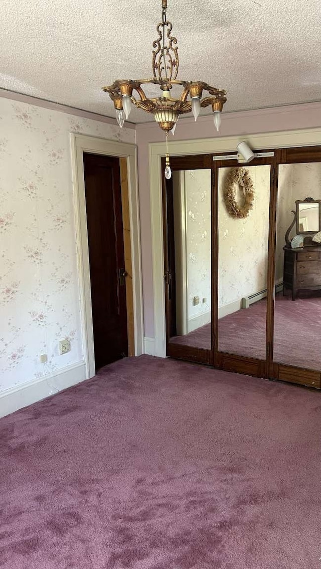 carpeted empty room featuring a textured ceiling, a baseboard heating unit, and a chandelier