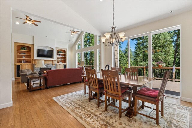 dining room featuring ceiling fan with notable chandelier, light wood-type flooring, high vaulted ceiling, and built in shelves