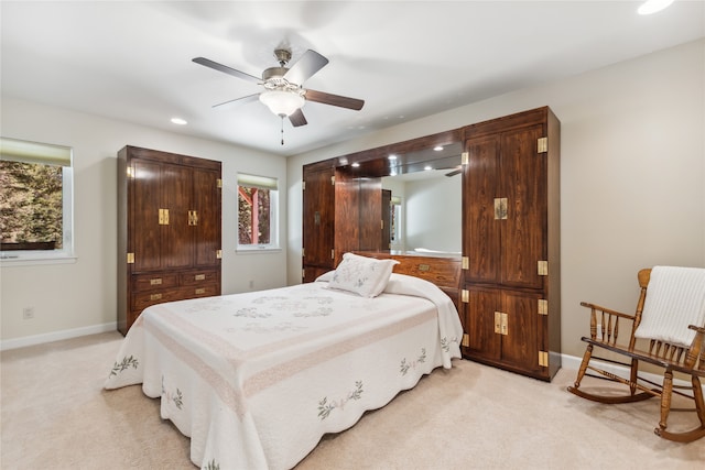 bedroom featuring light colored carpet, ceiling fan, and multiple windows