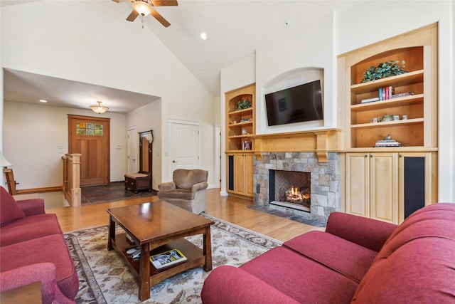 living room with high vaulted ceiling, ceiling fan, hardwood / wood-style flooring, and a stone fireplace