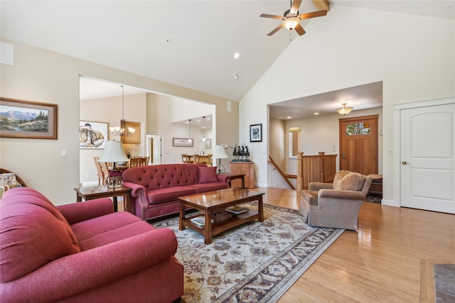 living room with light wood-type flooring, ceiling fan with notable chandelier, and high vaulted ceiling