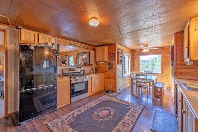 kitchen featuring gas stove, ceiling fan, black fridge, wood-type flooring, and wooden walls