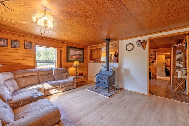 living room with light hardwood / wood-style floors, a wood stove, wooden walls, and wood ceiling