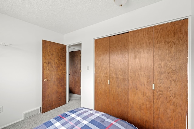 unfurnished bedroom with a closet, visible vents, carpet flooring, a textured ceiling, and baseboards