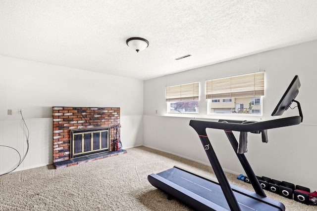 workout area with baseboards, visible vents, a textured ceiling, carpet floors, and a fireplace