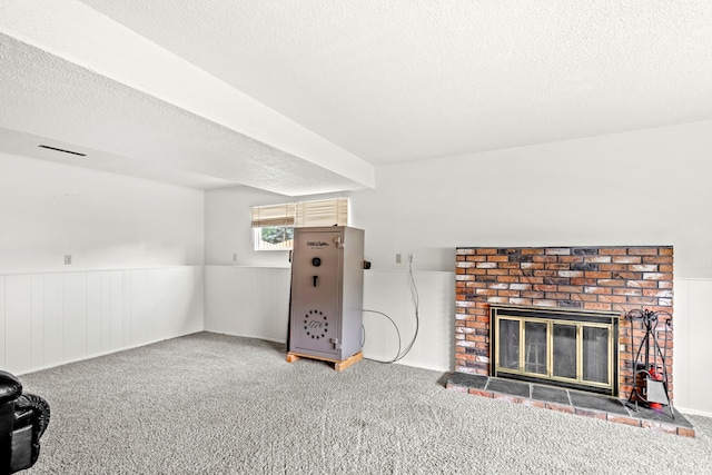 carpeted living room with a wainscoted wall, a fireplace, and a textured ceiling