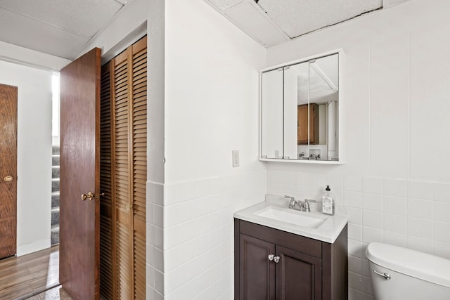 bathroom with tile walls, toilet, wainscoting, vanity, and wood finished floors