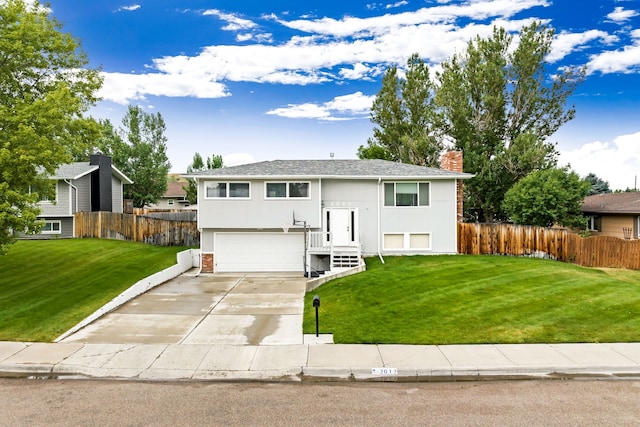 bi-level home featuring a garage, driveway, a front lawn, and fence