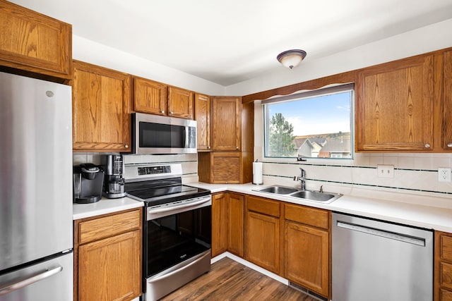 kitchen with stainless steel appliances, a sink, light countertops, backsplash, and brown cabinetry