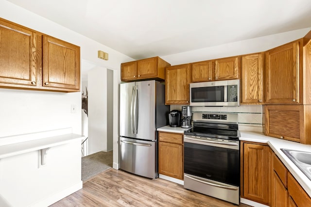 kitchen featuring brown cabinetry, appliances with stainless steel finishes, light countertops, light wood-type flooring, and a sink